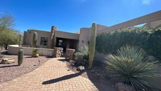 Desert-style home with stone walkway, cacti, and a bright blue sky.