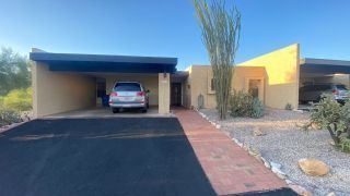 Modern house with a car in a covered driveway and desert landscaping under a clear sky