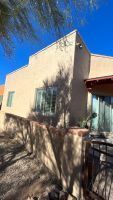 Stucco house exterior with a small window, wooden door, and desert shadows under a blue sky