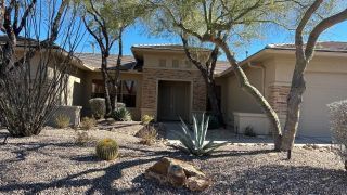 Desert-style house entry with rocks, agave, and leafless trees under a sunny sky