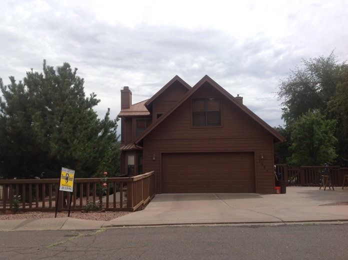 Brown house with a garage and wooden deck, framed by trees under a cloudy sky.