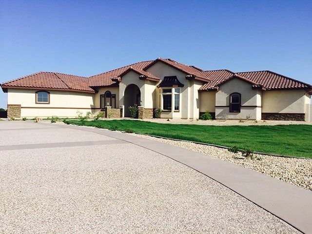 Large beige stucco house with a red tile roof and curved driveway under a clear blue sky