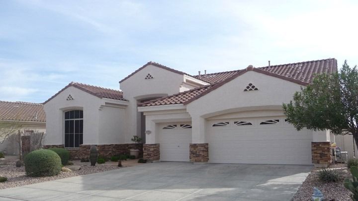 Suburban house with beige stucco, red tile roof, three garage doors, and desert landscaping