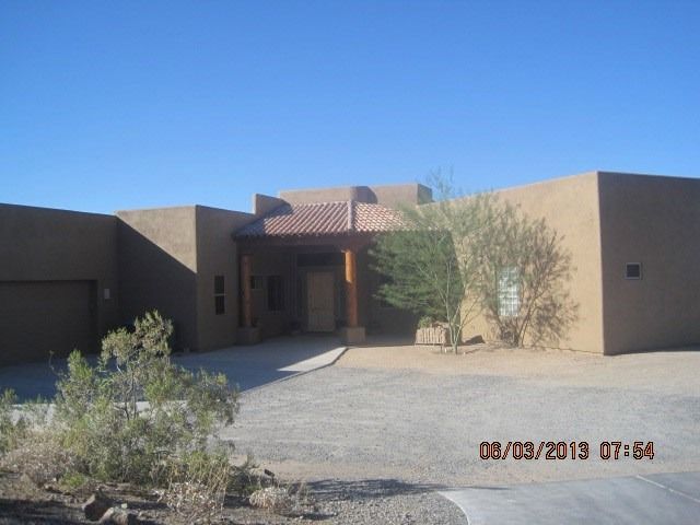 Adobe-style tan house entrance with desert landscaping under a clear blue sky