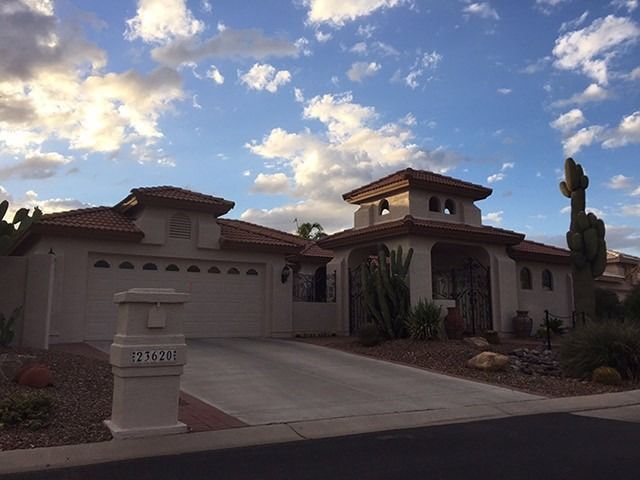 Modern beige stucco house with a two-car garage, front yard, and a sunset sky with clouds