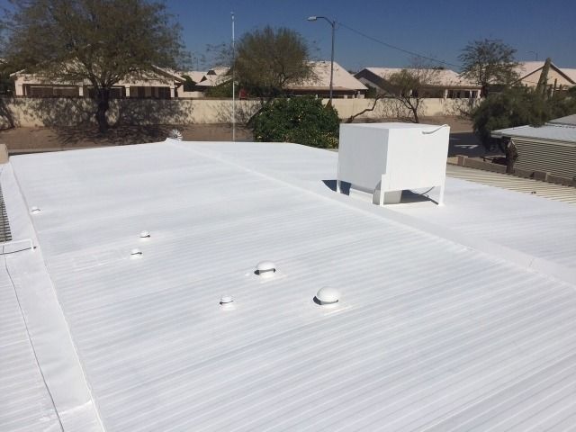 White flat roof with vents and a rooftop HVAC unit in a suburban backyard.
