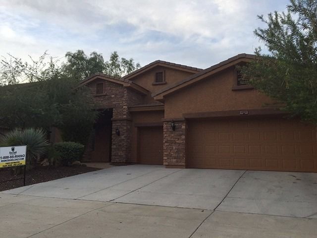 Brown suburban house with a two-car garage and a wide concrete driveway.