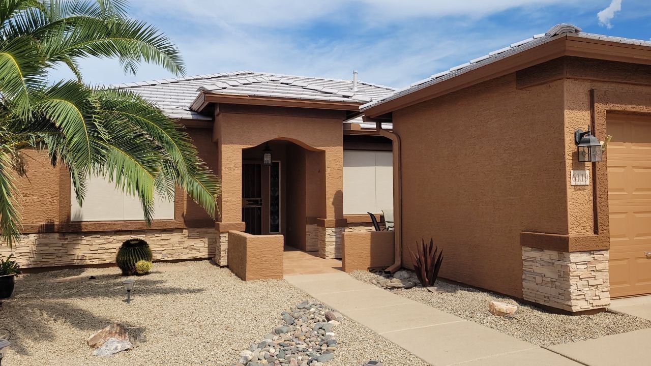 Front view of a tan stucco house with a tiled roof, desert landscaping, and a palm tree by the walkway