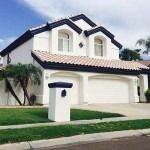 Suburban two-story white house with a red-tiled roof, garage, and manicured lawn.