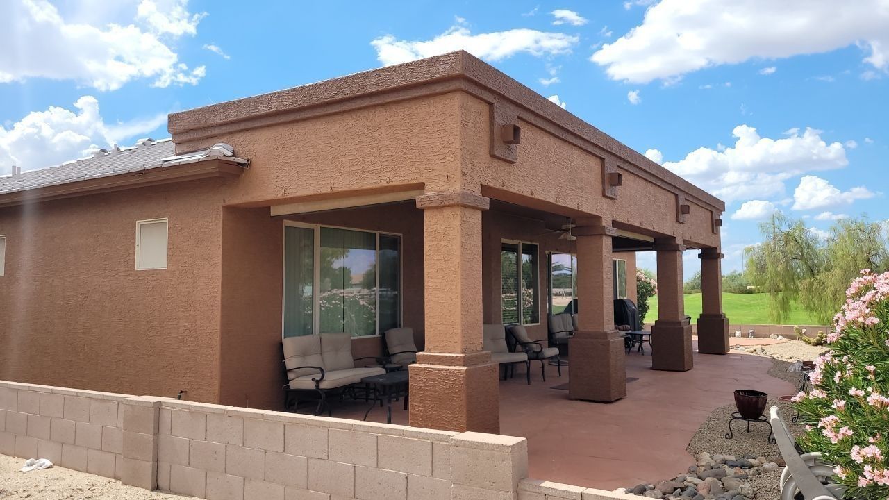 Adobe-style house with covered porch, tan stucco walls, and desert landscaping under a blue sky