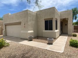 Tan stucco house exterior with a garage, front entry, and desert landscaping under a clear sky