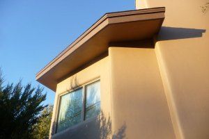 Beige house exterior with a window and sloped roof against a blue sky