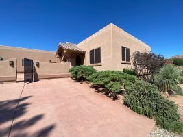 Modern tan stucco house with desert landscaping and a wide driveway under a clear blue sky