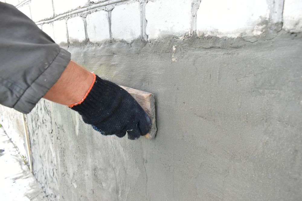 Gloved hand smoothing wet gray concrete on a wall with a trowel