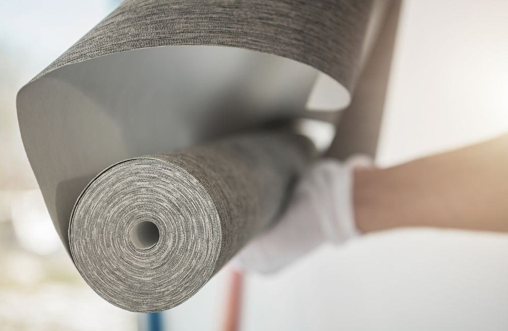 Close-up of a rolled gray carpet being unrolled by gloved hands