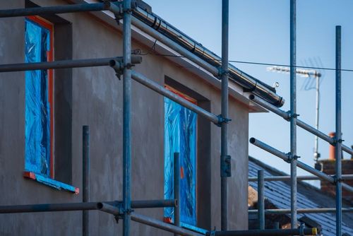 Scaffolding outside a house with blue-covered windows during construction