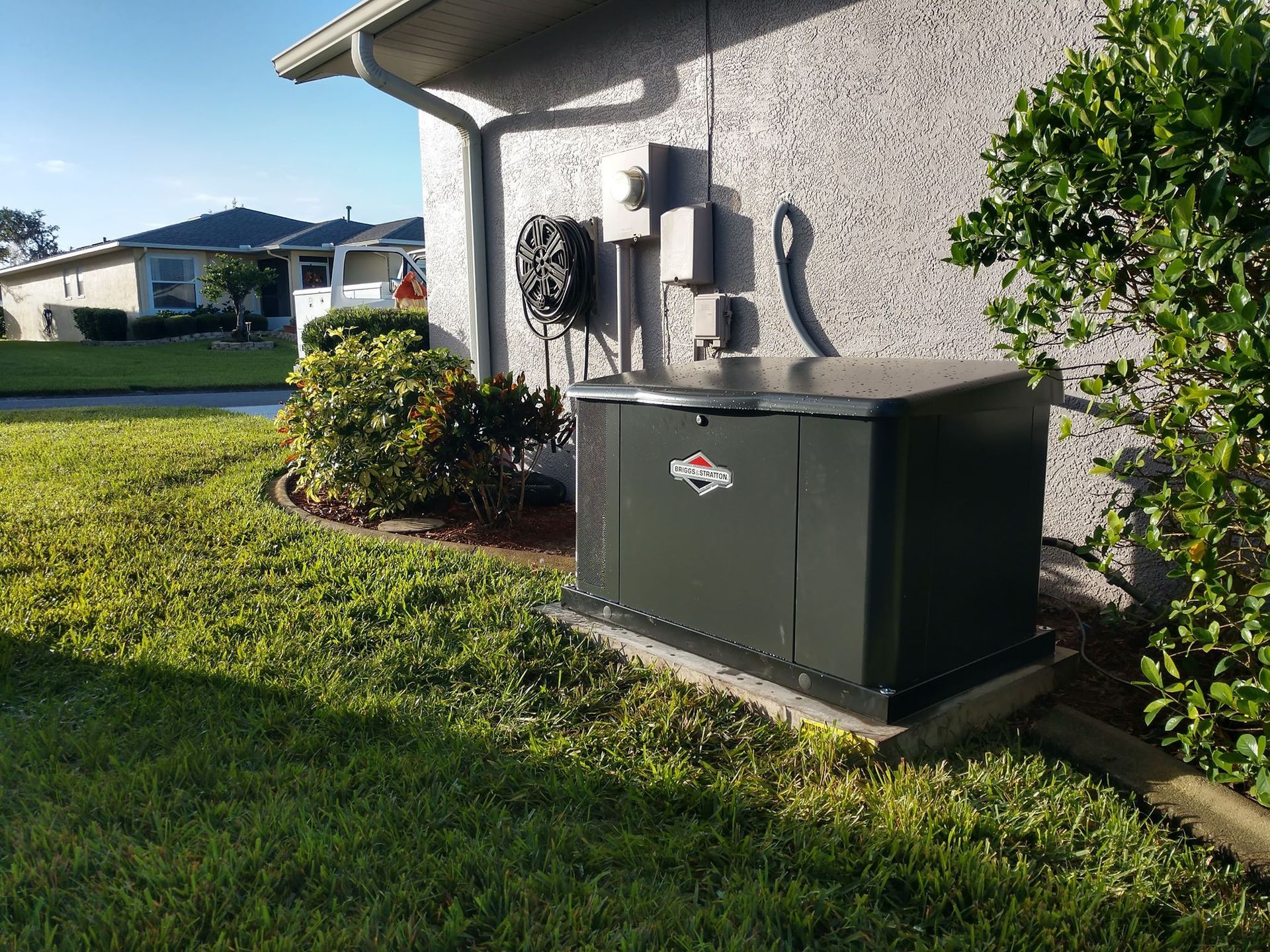 Green standby generator next to a house with beige stucco siding, on a grassy lawn.