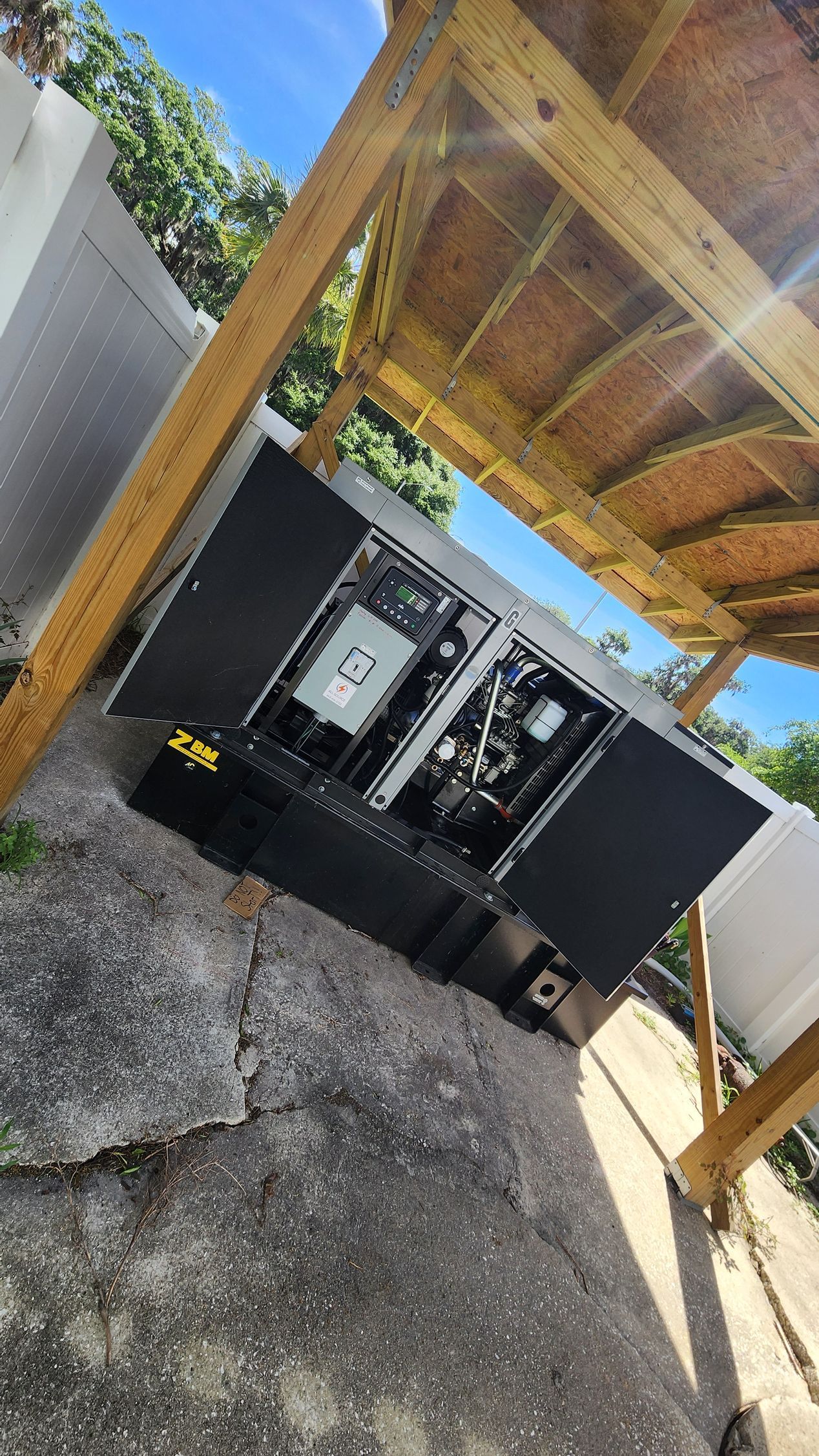 Gray generator with open doors, under a wooden structure, outdoors.
