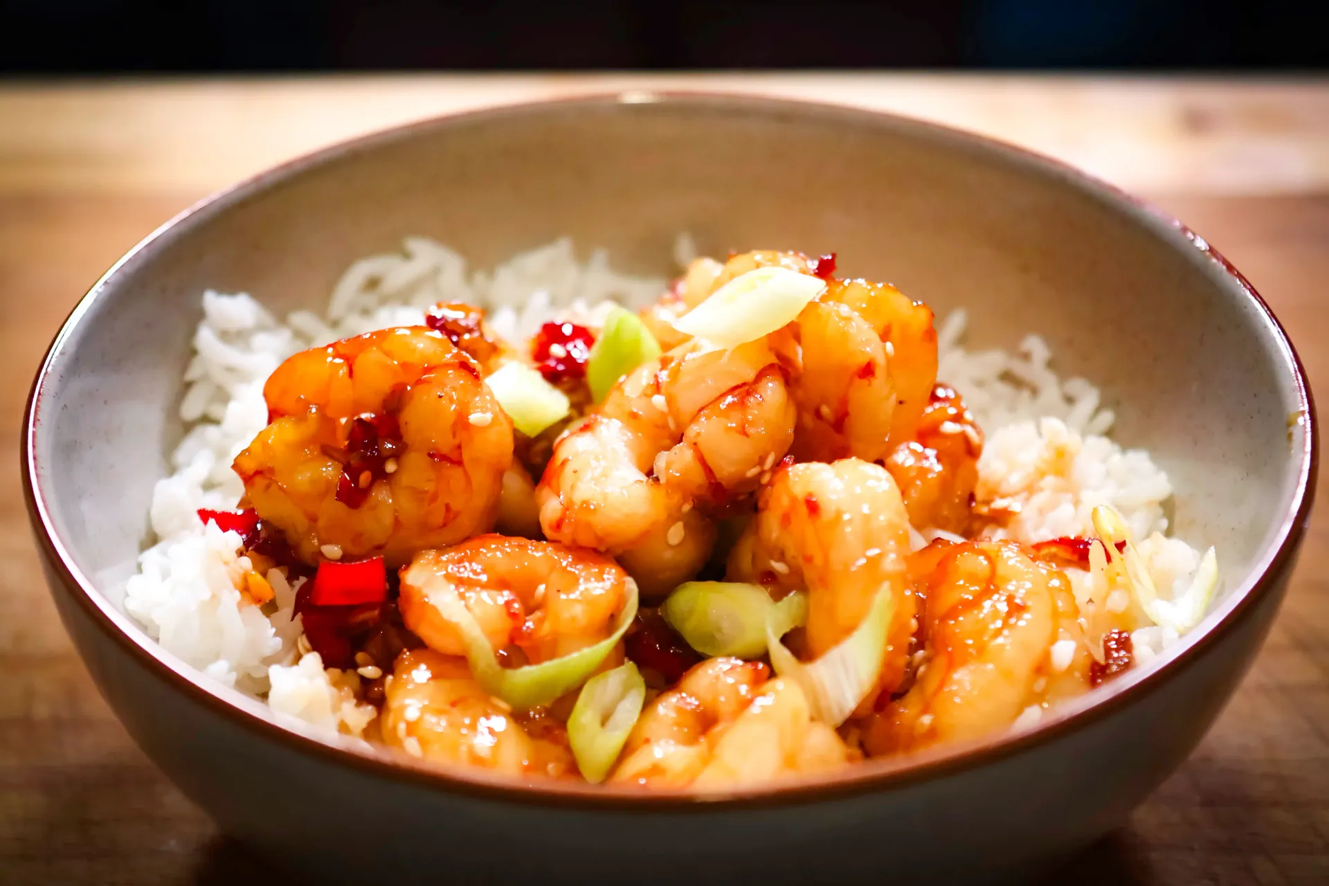 Cooked shrimp in orange sauce, held with chopsticks, in a black bowl.