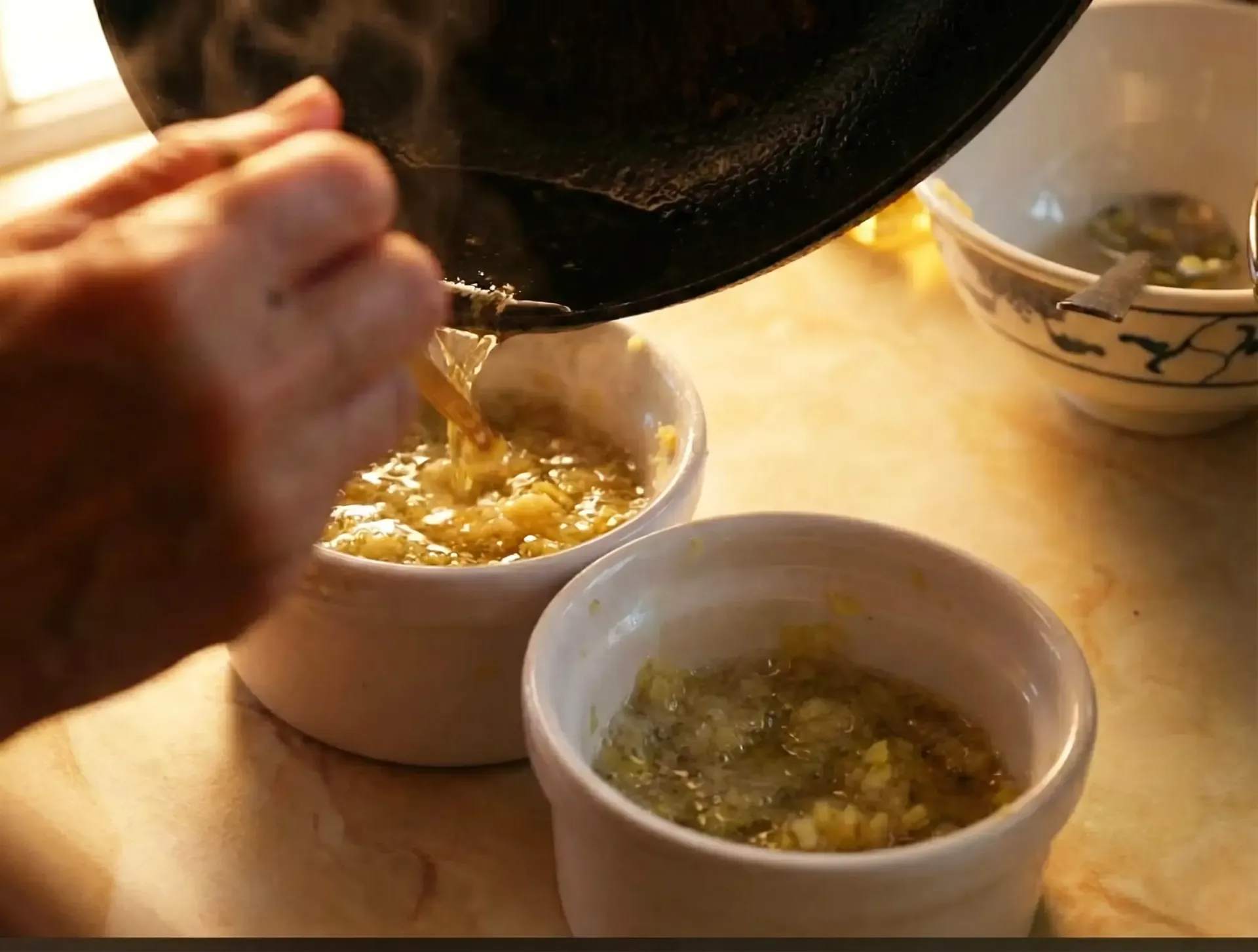 Person pouring liquid from a pan into two white ramekins with a yellowish-green mixture inside.