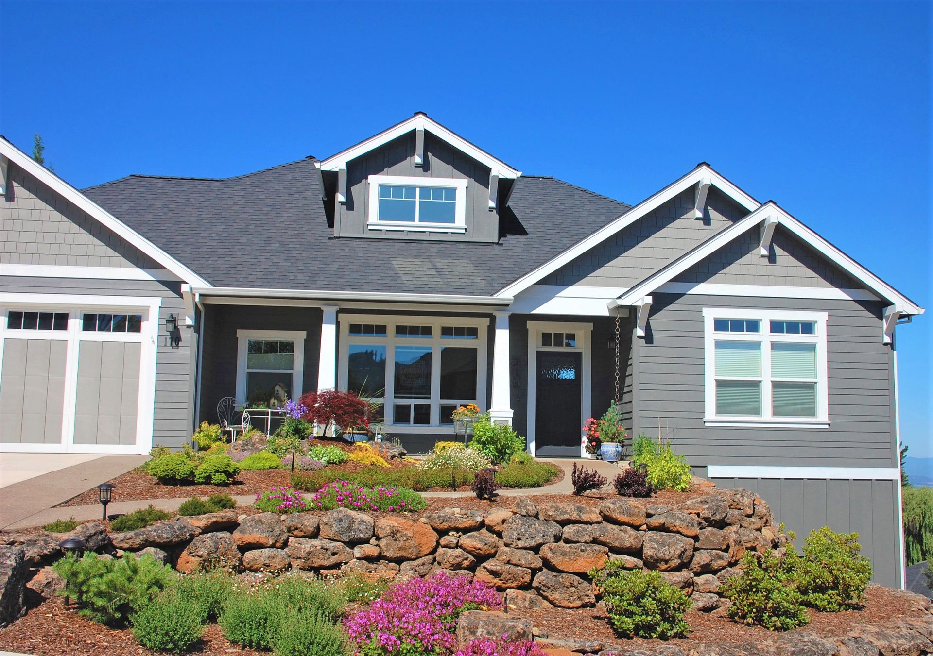 Gray suburban house with blue trim and stone front landscaping under a bright blue sky
