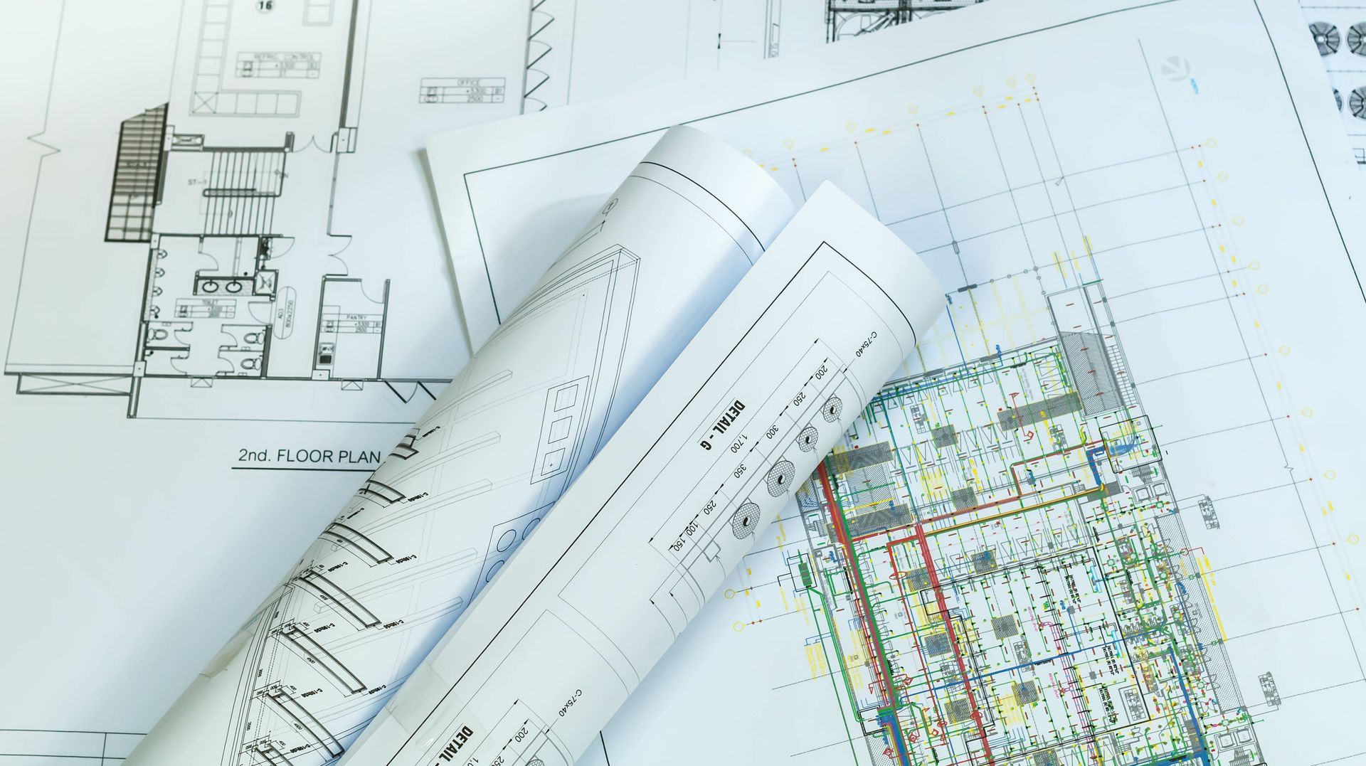 Rolled architectural blueprints over detailed building plans on a drafting table