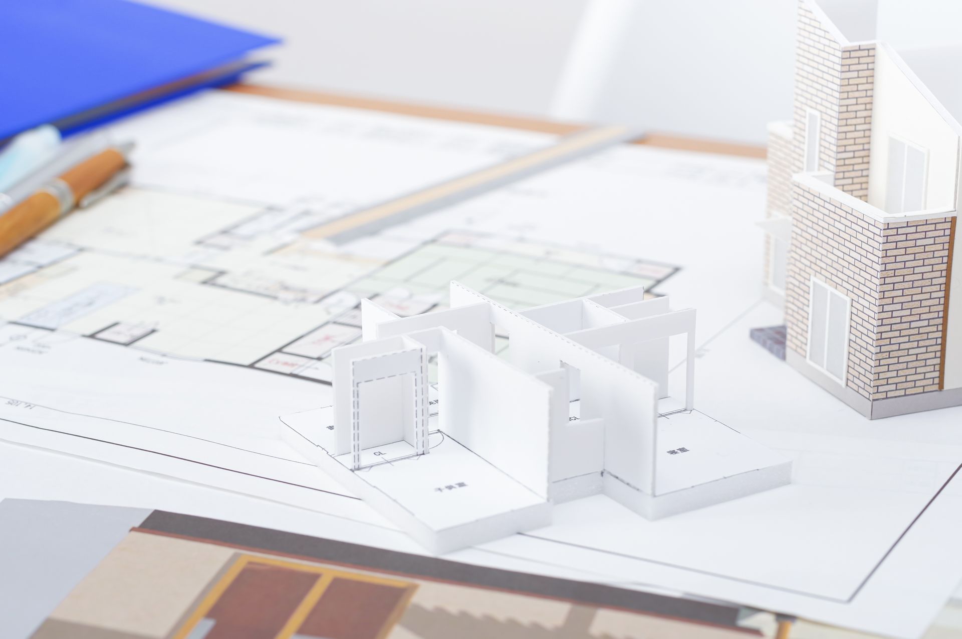 Architectural scale model on blueprints beside a pencil and building renders