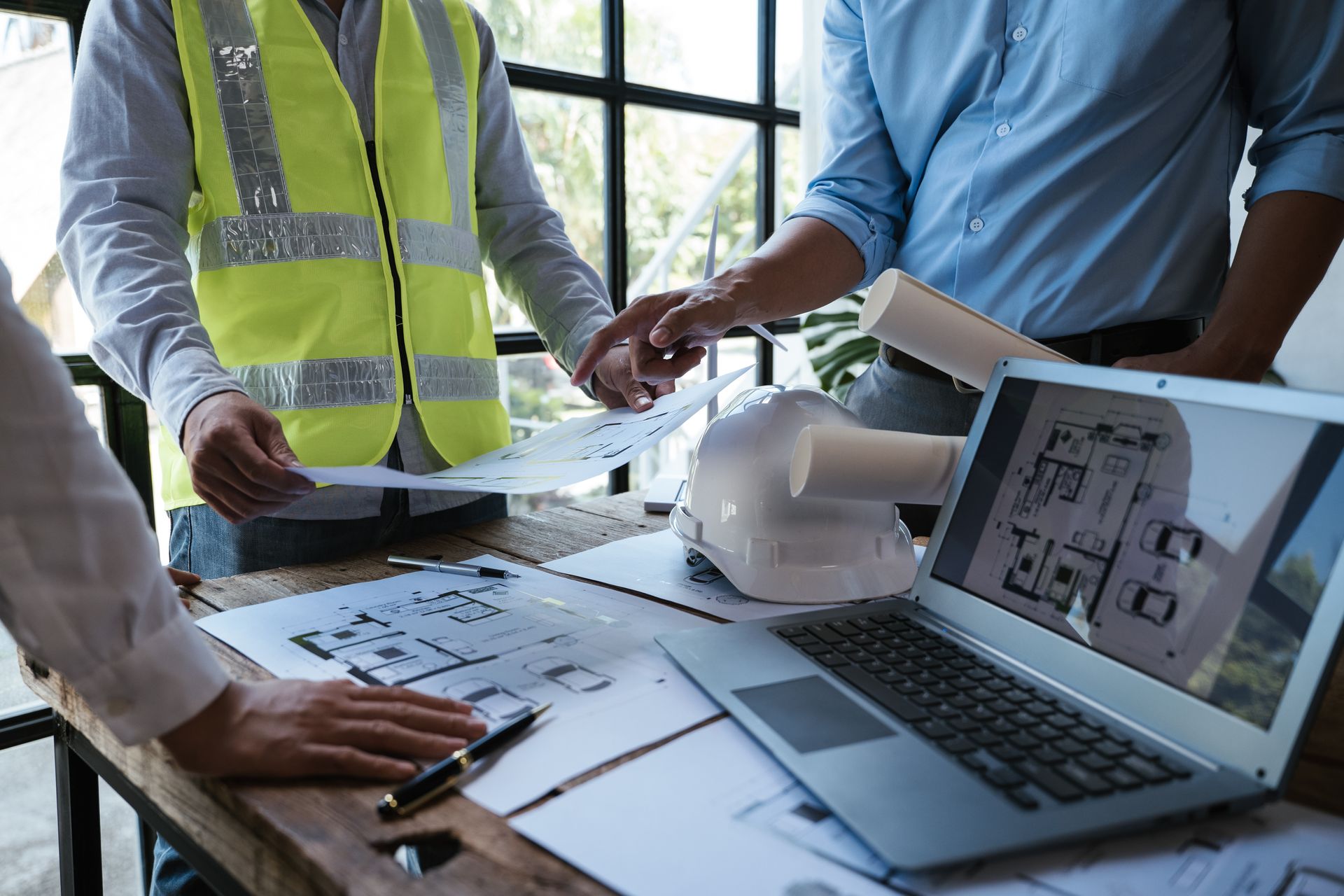 Colleagues reviewing building plans and laptop schematics at a worksite table Colleagues reviewing building plans and laptop schematics at a worksite table