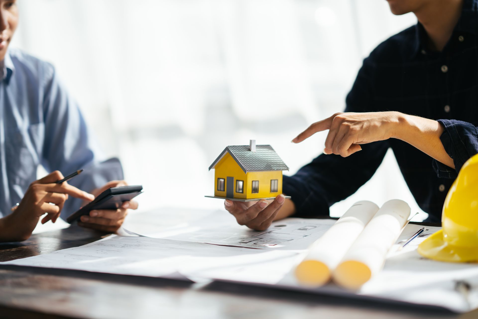 People reviewing a small house model and documents at a table during a real estate meeting People reviewing a small house model and documents at a table during a real estate meeting