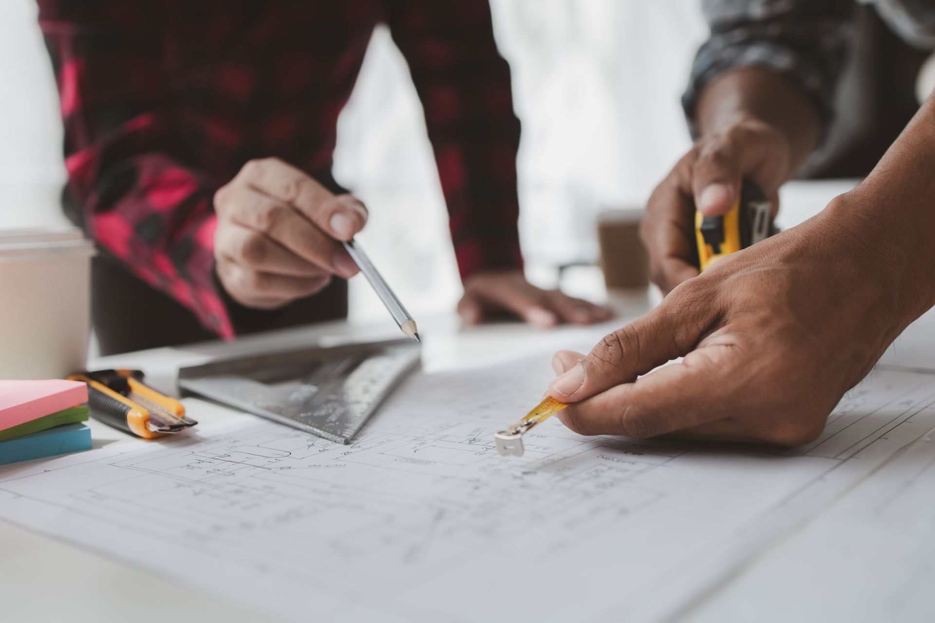 Hands sketching on a floor plan with a ruler, pencil, and calculator on a desk Hands sketching on a floor plan with a ruler, pencil, and calculator on a desk