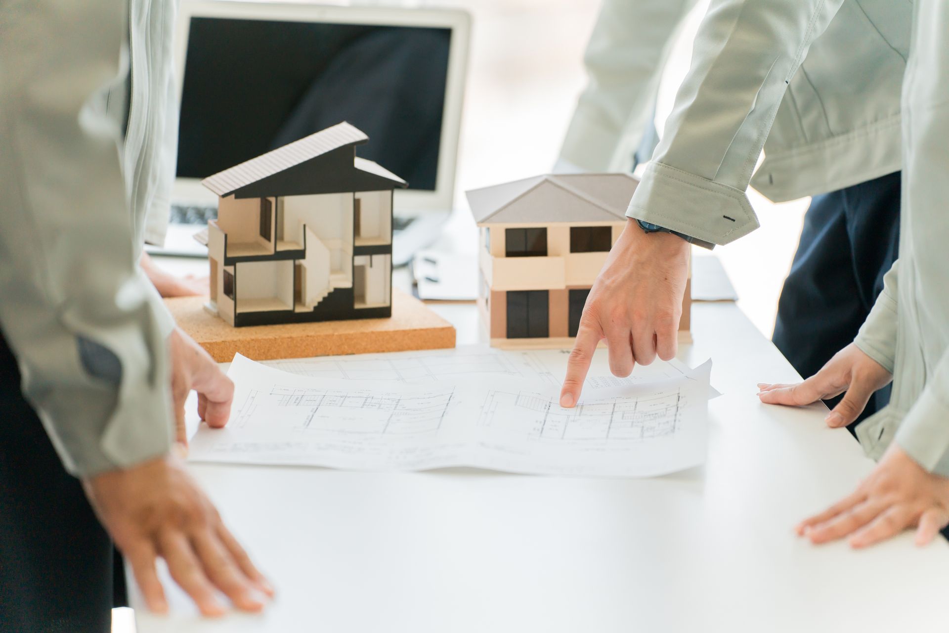 Hands reviewing house models and architectural plans on a bright office table