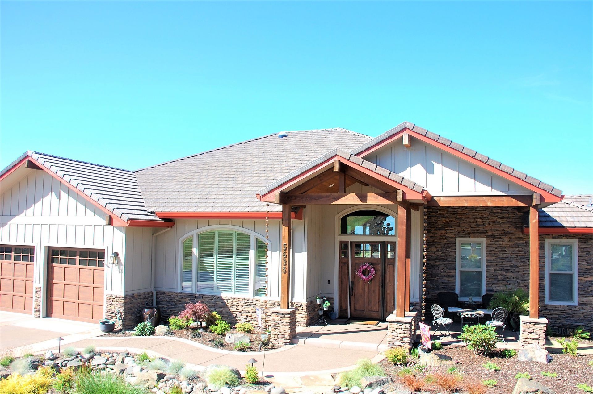Suburban single-story house with stone and wood facade, garage, and landscaped front yard under a blue sky