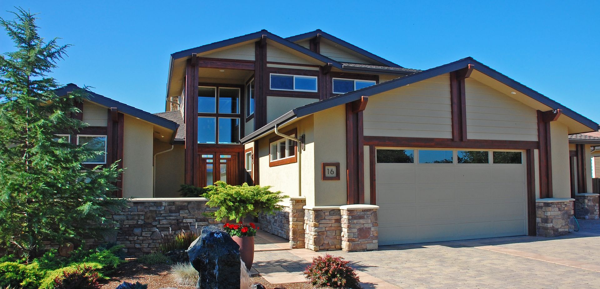 Modern two-story suburban house with tan siding, stone accents, and a double garage under a blue sky Modern two-story suburban house with tan siding, stone accents, and a double garage under a blue sky