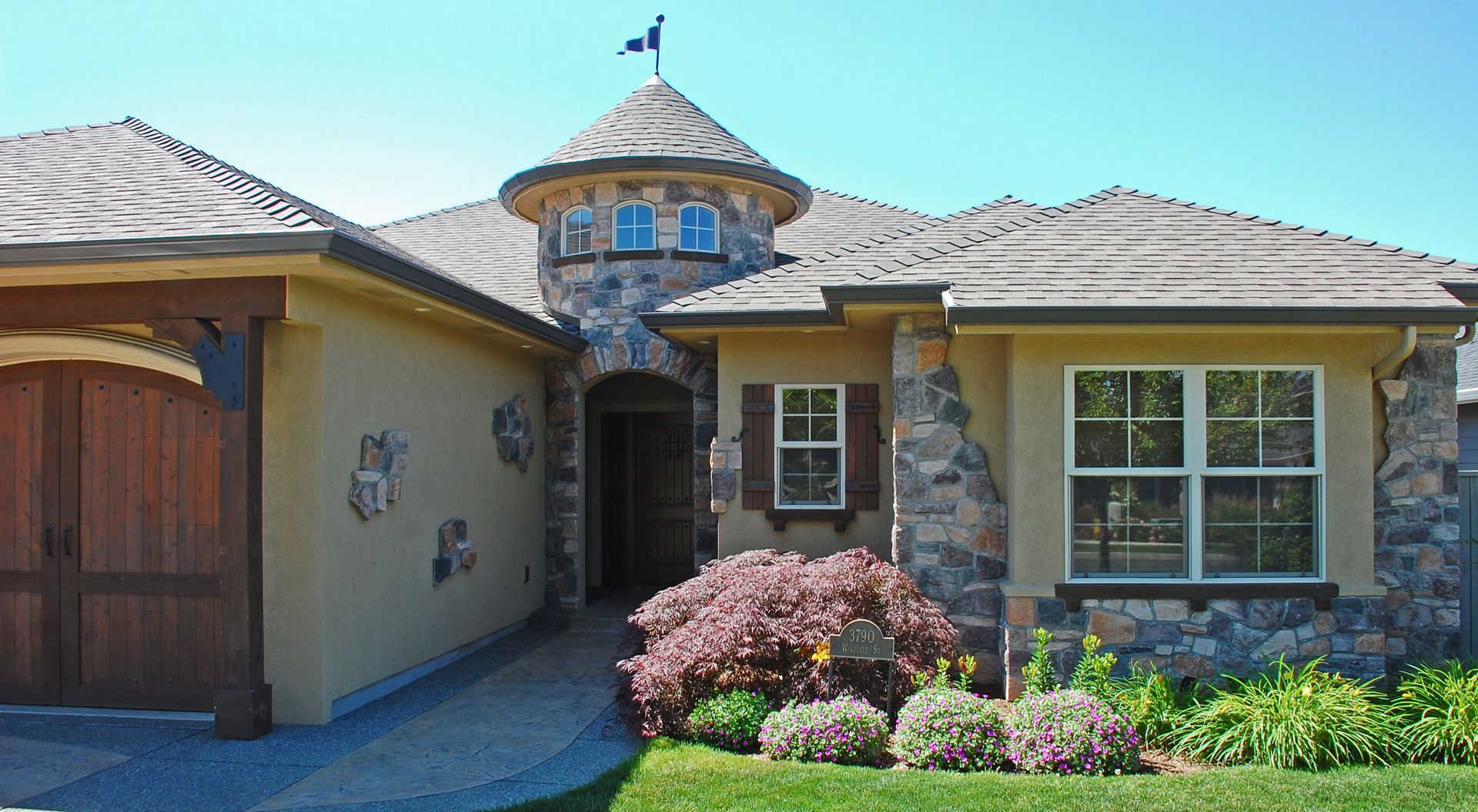 Suburban stucco house with a stone entry, garage, and landscaped front yard under a bright sky Suburban stucco house with a stone entry, garage, and landscaped front yard under a bright sky