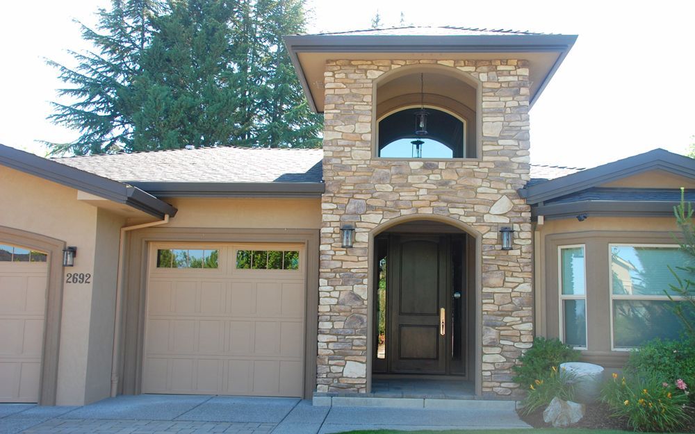 Modern stone house entrance with arched entryway, garage, and front porch under bright daylight