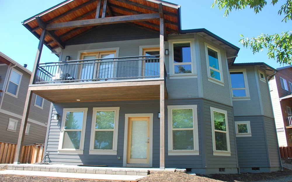 Two-story gray house with a covered balcony and large windows in bright daylight