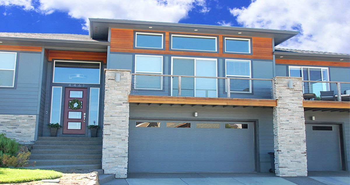 Modern two-story townhouse with stone facade, large windows, and two garage doors under a blue sky