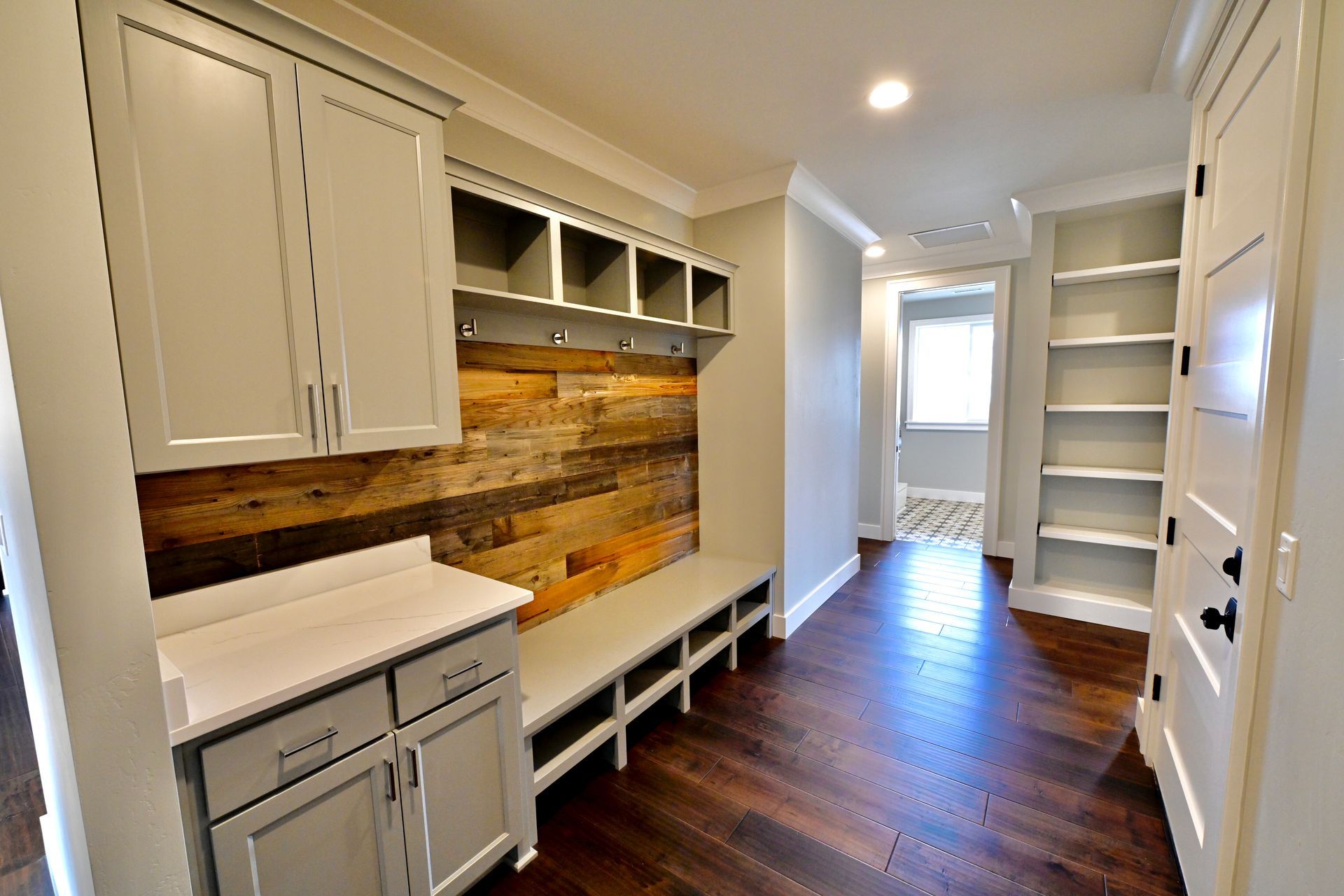 Bright hallway laundry room with white cabinets, wood accent wall, and dark hardwood floors