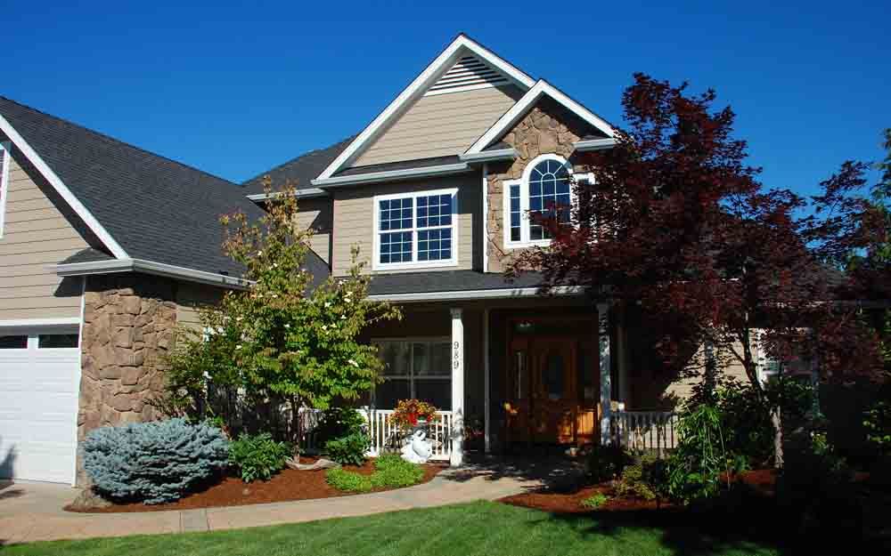 Suburban house with brick exterior, front porch, and landscaped yard in sunlight