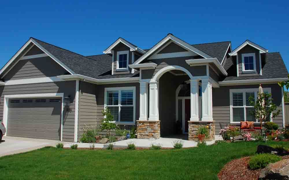 Modern suburban house with gray siding, stone accents, and a two-car garage under a blue sky