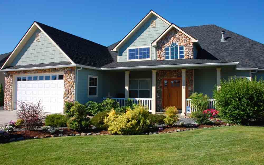 Suburban house with stone facade, blue siding, white garage, and landscaped front yard