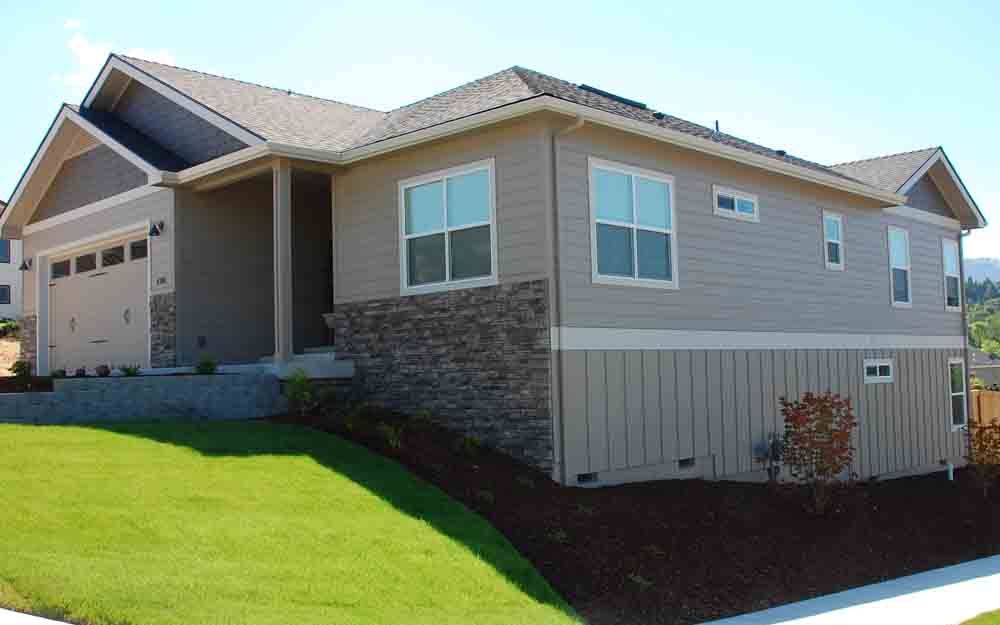 Single-story beige house with stone accents and a garage on a sloped green lawn