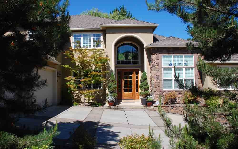 Front view of a tan stucco house with arched entry, wooden double doors, and landscaped front walkway