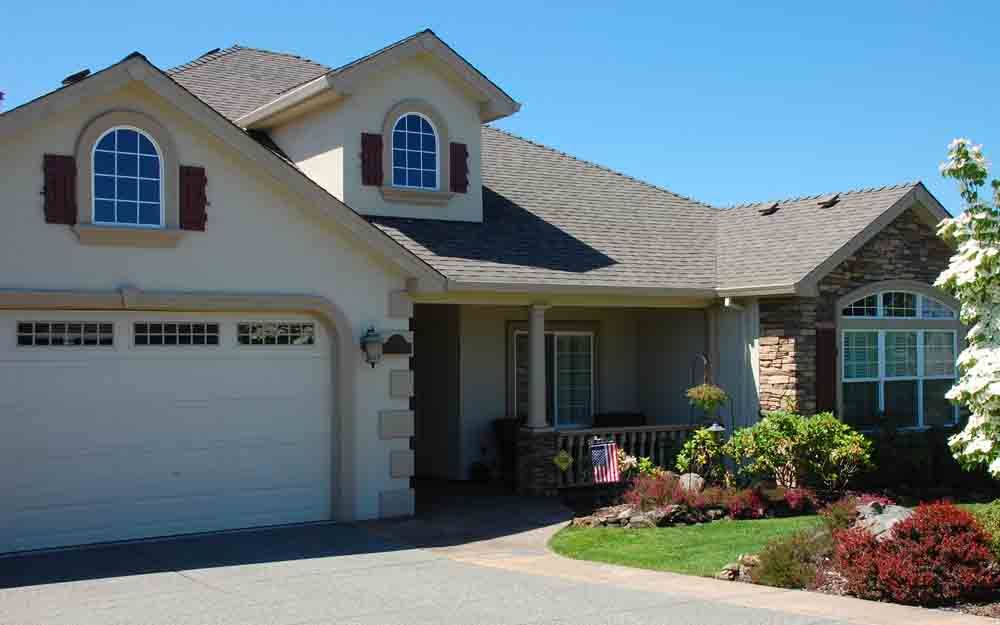Suburban house with two-car garage, arched windows, and landscaped front yard under a clear blue sky