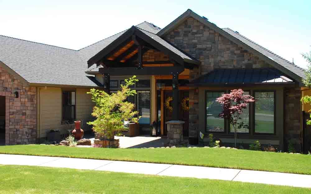 Suburban brick house with gabled roof, stone entrance, and manicured lawn on a sunny day