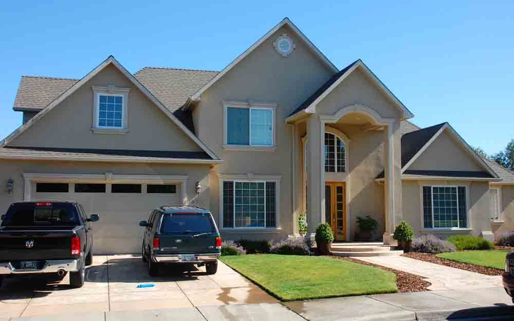 Suburban two-story house with beige siding, two black SUVs in the driveway, and a manicured lawn