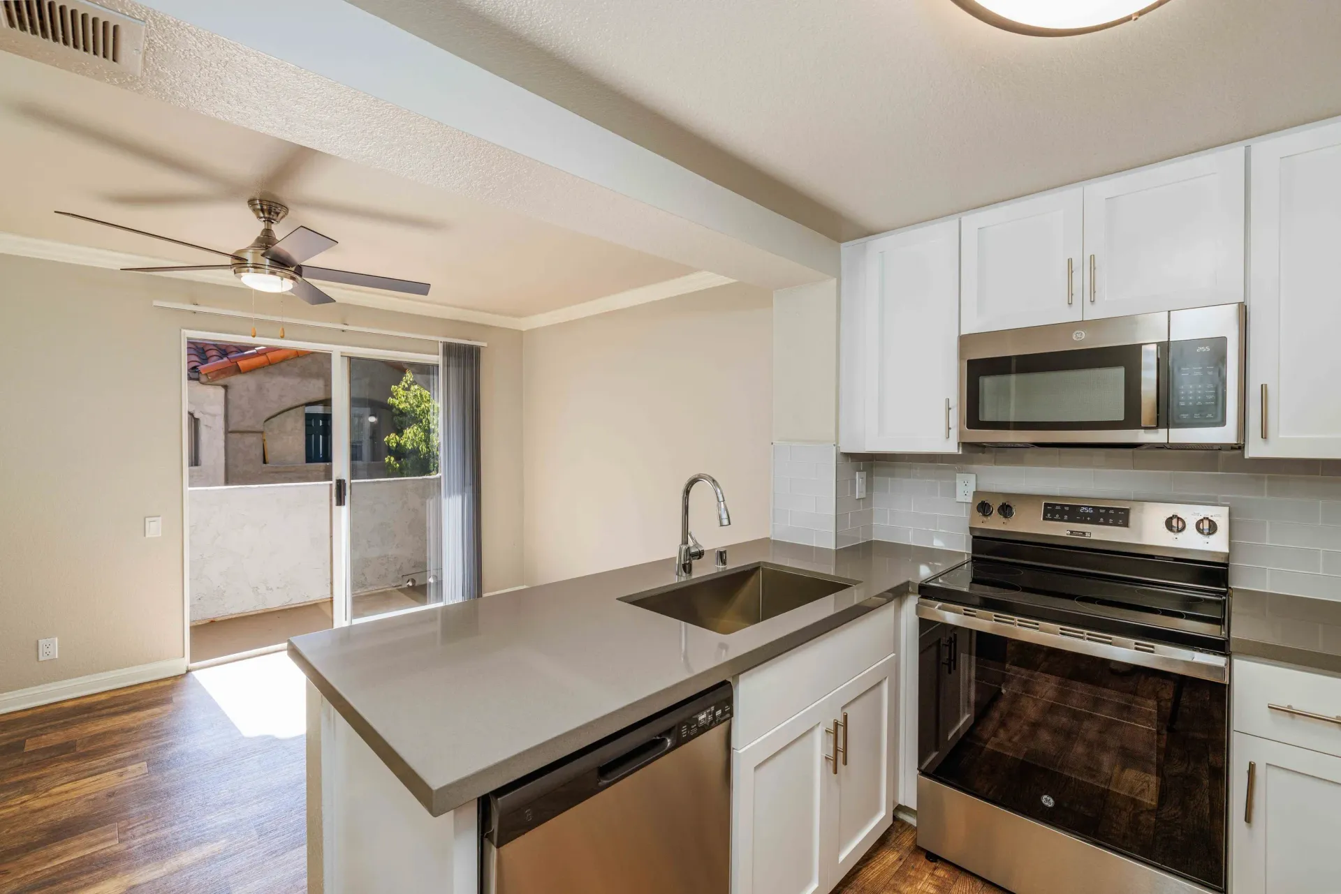 Modern kitchen with island, stainless steel appliances, white cabinets, and sliding balcony door.