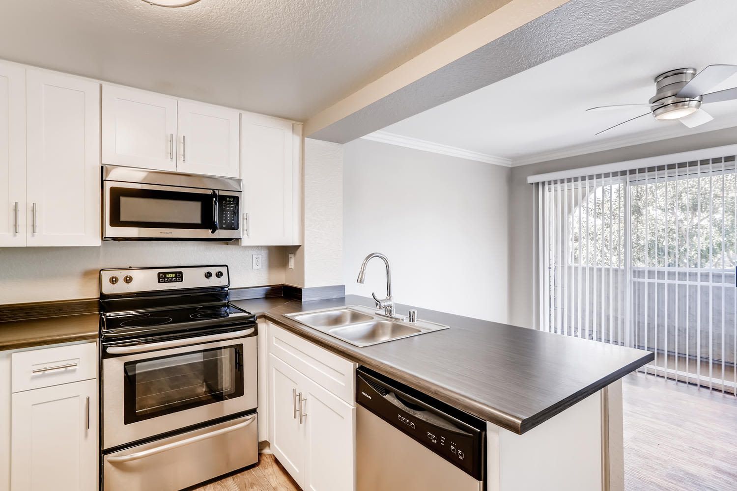 Apartment kitchen with white cabinets, stainless steel stove and microwave, and a double sink.