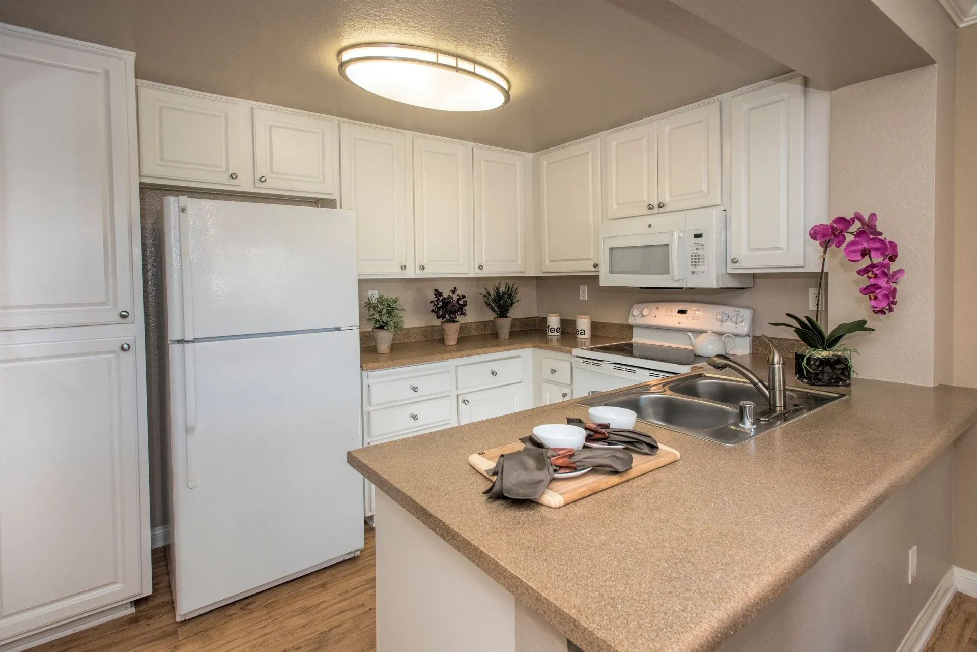 White kitchen with island counter, double sink, and white appliances.