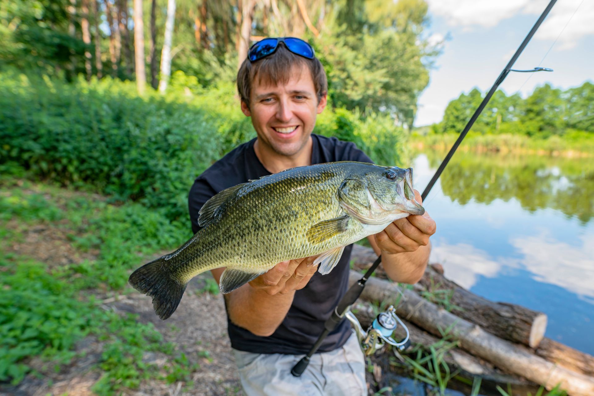 A man is holding a large fish in his hands next to a lake.